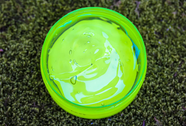 Aloe vera gel in a round jar against a green moss background top view. Green transparent liquid cream for moisturising the body, face. Care basic no label cosmetic product. Soothes skin after sunburn. - Photo, Image