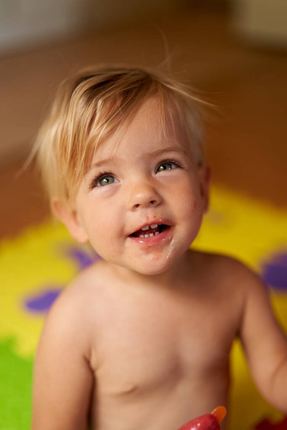 Riendo niño pequeño con la cara sucia y helado en la mano se sienta en el suelo - Foto, Imagen
