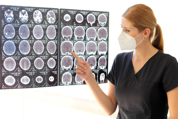 女性の神経科医は頭トモグラフィーをレビューし、病院のマスクで作業します - 写真・画像