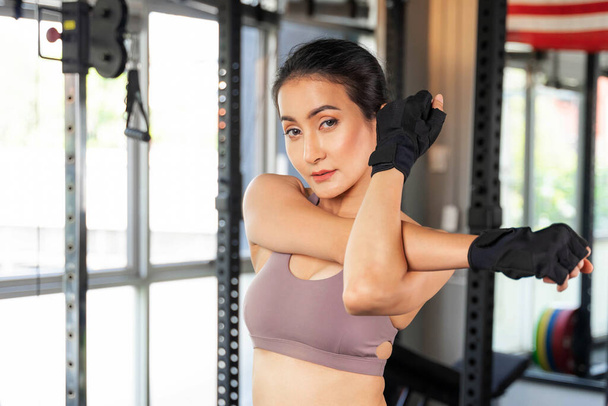 Hermosa mujer de fitness slim fit en ropa deportiva estirando su brazo en una sala de gimnasio, cuerpo delgado chica sexy asiática estilo de vida concepto de fitness mujer saludable - Foto, imagen