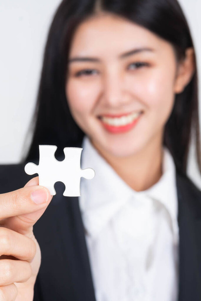 Business woman holding and showing a jigsaw puzzle piece over isolated white background , selective focus, blurred - business concept  - Photo, Image