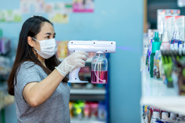 Asian staff wearing gloves using electric Alcohol Nano Spray Gun Handhold Blue Light Disinfectant Spray. prevent infection Covid-19 in the shop. concept healthcar - Photo, Image