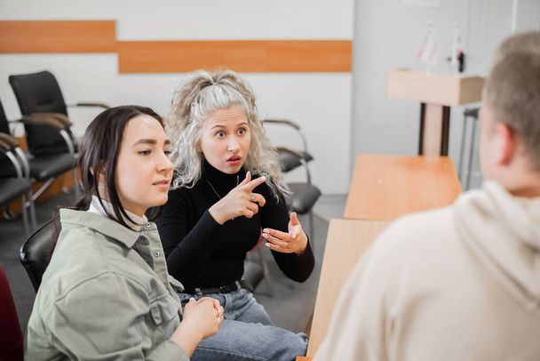 Two girls and a guy are talking in sign language. Three deaf students chatting in a university classroom. - 写真・画像