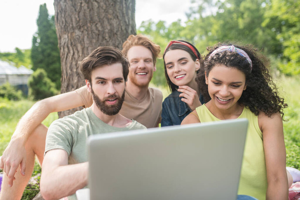 Four young happy friends looking at laptop - Photo, image