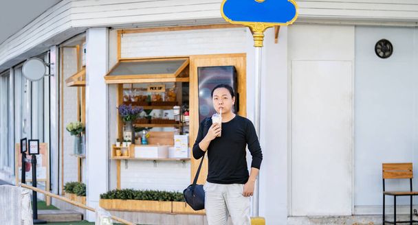 Aasialainen mies mustassa t-paidassa pitää kuplapalloa jäällä Maitotee myymälän edessä ulkona kadulla kävelypolulla. - Valokuva, kuva