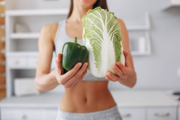 Beautiful and sporty girl in a kitchen with a vegetables - Foto, Imagem