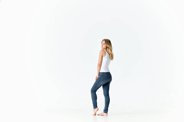 жінка в джинсах стоїть босоніж на підлозі позує модний світлий фон
 - Фото, зображення