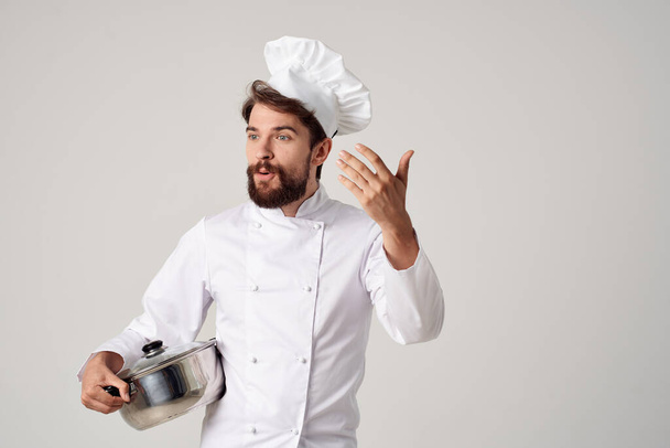 een man in een koks uniform een pan in zijn handen proberen voedsel werk - Foto, afbeelding