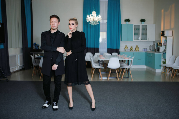 Young stylish man and woman in black clothes posing while standing in the interior. Fashionable outfit. Life style. Elegance. - Foto, afbeelding