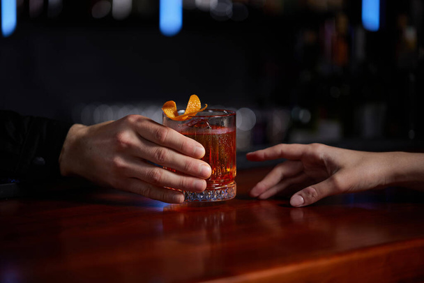 Barman holding out glass with alcoholic cocktail to the client - 写真・画像