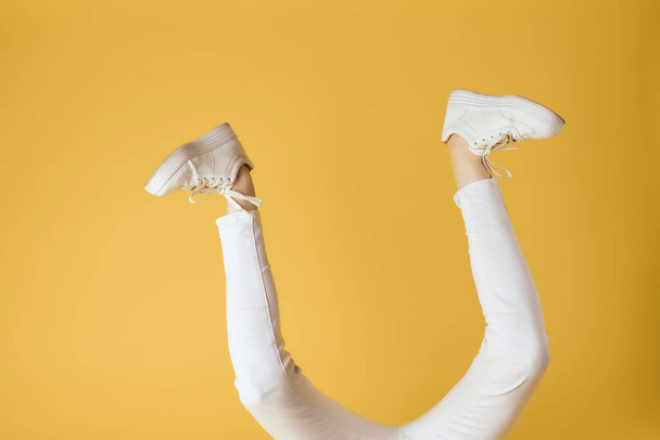 piernas invertidas en zapatillas blancas moda estilo moderno fondo amarillo - Foto, Imagen