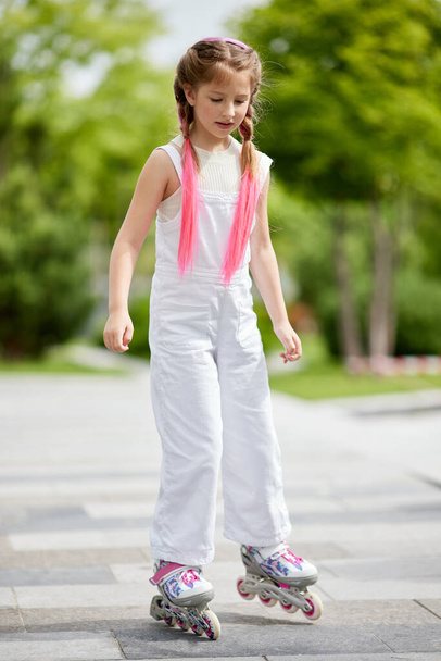 Cheerful little girl on roller skates with braided hair style - Foto, afbeelding