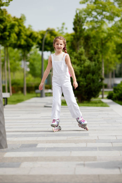 Cheerful little girl on roller skates with braided hair style - Foto, imagen