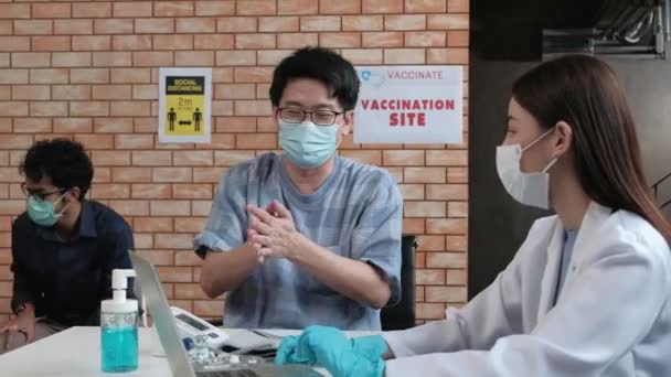Sociale afstandelijkheid Aziaten Mensen dragen gezichtsmaskers wachtrij voor preventie coronavirus (COVID-19) vaccinaties na medische campagne in een ziekenhuis kliniek tegen een oranje bakstenen muur achtergrond. - Video