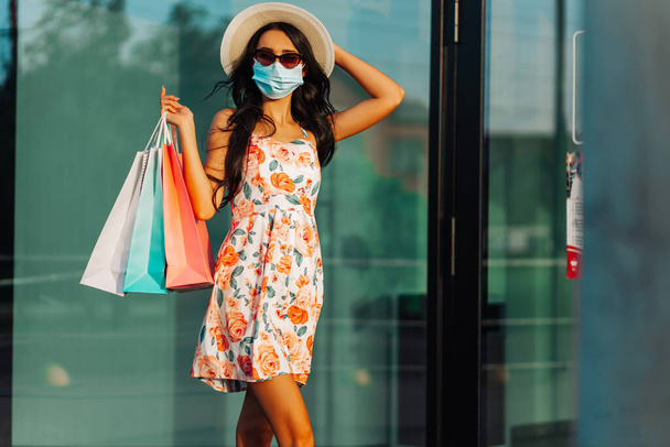 Young happy woman in medical protective mask, from protection of coronavirus, with bags, walking down the street, Shopping concept, quarantine, coronavirus - Фото, изображение
