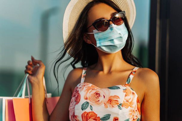 Молода щаслива жінка в медичній захисній масці, від захисту коронавірусу, з сумками, що йдуть по вулиці, концепція покупок, карантин, коронавірус
 - Фото, зображення