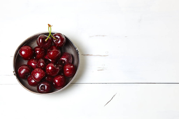 Sweet cherries in a metal bowl on wooden background, closeup. Fresh ripe sweet cherries in a bowl with droplets of water, top view - 写真・画像