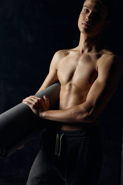 athlete in pants nude torso fitness mat black background - Foto, Imagem