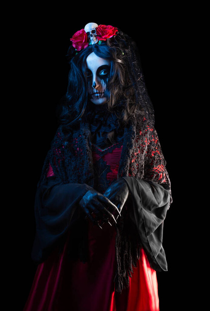 Mysterious woman with Santa Muerte makeup in shawl and crown with skull and roses on black background. Halloween concept. - Photo, Image