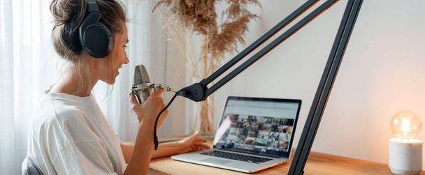 Woman podcaster streaming and broadcasting her podcast from homemade studio. Female recording podcast from home and talking into a microphon - Photo, image
