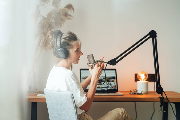 Woman radio host recording podcast at home studio. Female podcaster recording broadcasting into microphone using laptop - Фото, изображение