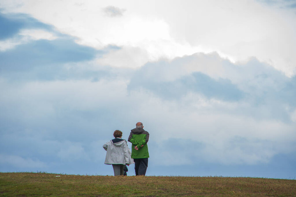 An old couple walking in the field in a cloudy weather - Zdjęcie, obraz