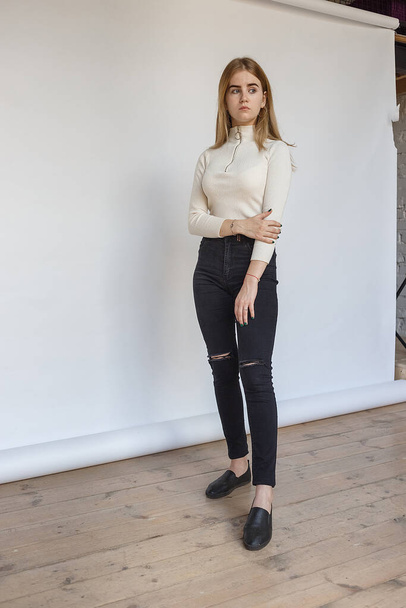 Porträt eines jungen durchdachten Teenie-Models in weißem Pullover und schwarzer Jeans - Foto, Bild