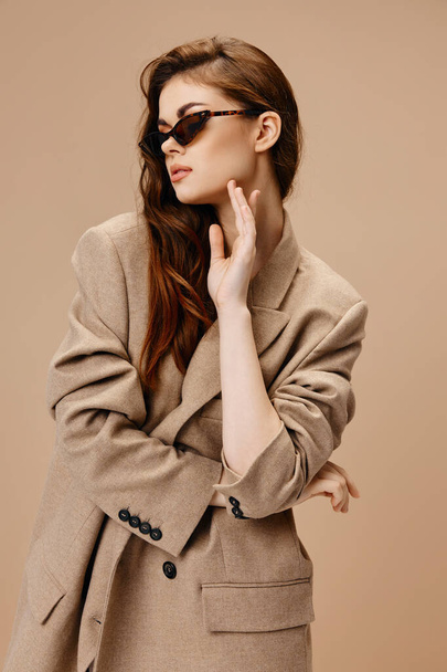 retrato de mujer elegante con gafas maquillaje abrigo fondo beige - Foto, Imagen