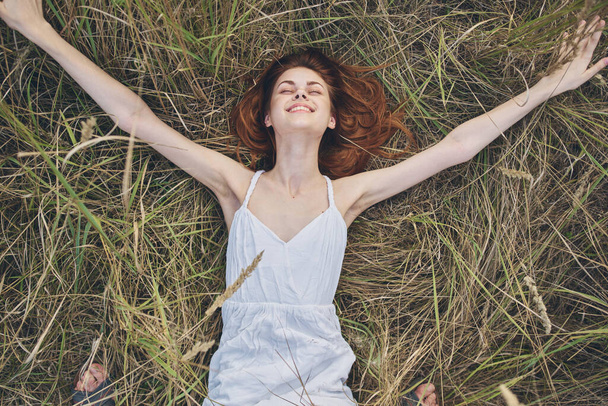 Een vrouw in een witte jurk ligt op het gras natuur ontspanning zon top uitzicht - Foto, afbeelding
