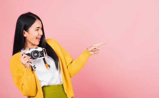 Attractive energetic happy Asian portrait beautiful cute young woman teen excited smiling holding vintage photo camera and pointing finger to side space, studio shot isolated on pink background - Фото, зображення