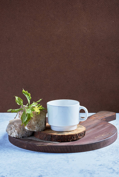 A vertical shot of a white cup on a wooden surface with rocks and a twig - Φωτογραφία, εικόνα