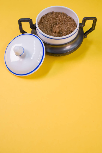 A vertical shot of brown sugar in a small ceramic jar on a yellow table - Fotó, kép