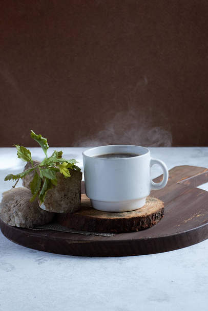 A vertical shot of a cup of coffee on a wooden board with rocks and a twig - Φωτογραφία, εικόνα
