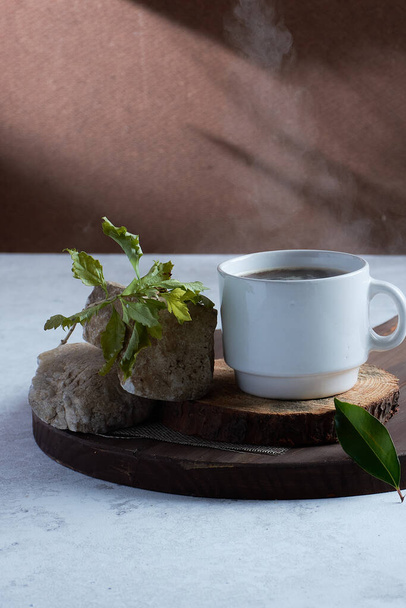 A vertical shot of a cup of coffee on a wooden board with rocks and a twig - Фото, зображення