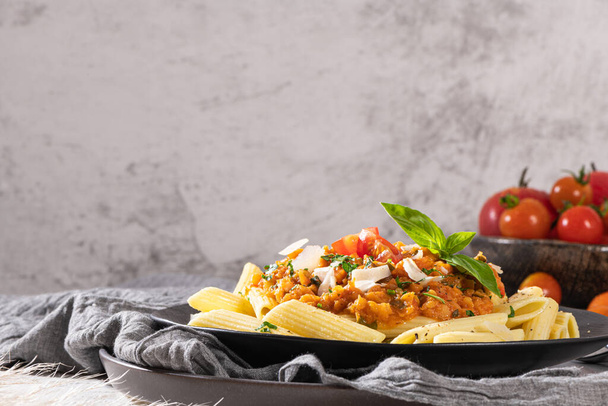 Tasty appetizing classic italian penne pasta with vegetarian lentil bolognese sauce, cheese parmesan and basil on plate on light table. Healthy eating concept. - Photo, Image