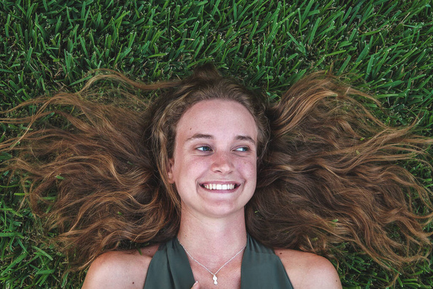 Mooi meisje met lang wit haar ligt op groen gras en glimlacht - Foto, afbeelding
