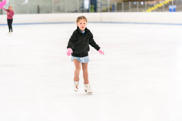 Mała dziewczynka ćwicząca łyżwy figurowe na krytym lodowisku. - Zdjęcie, obraz