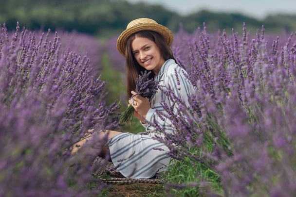 紫の花のフィールドの背景にラベンダー花束を持つ若い女性 - 写真・画像
