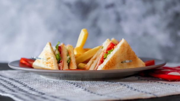Club sandwich, 4 slices laid out on a gray plate with tomatoes and fries - Photo, Image