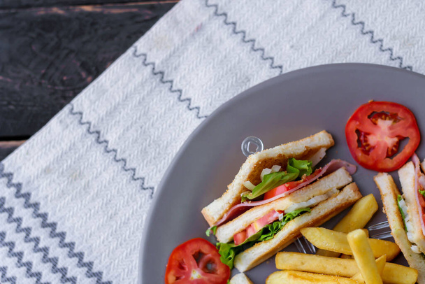 Клубний бутерброд, 4 скибочки викладені на сірій тарілці з помідорами та картоплею
 - Фото, зображення