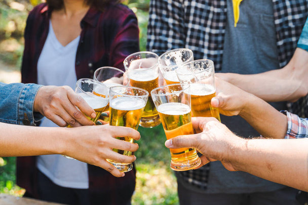 Foto recortada de personas sosteniendo vasos de cerveza celebrando en la fiesta de campamento de verano al aire libre. Amigos tintineo botella de cerveza durante el camping al aire libre - Foto, imagen