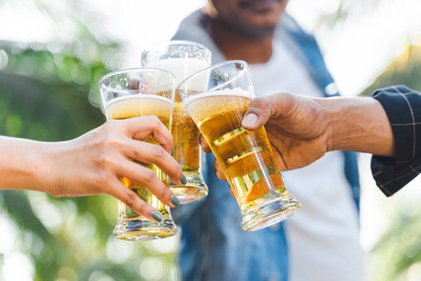Cropped shot of people holding beer glasses celebrating in the summer camping party outdoor. Friends clinking bottle of beer during camping outdoor - 写真・画像