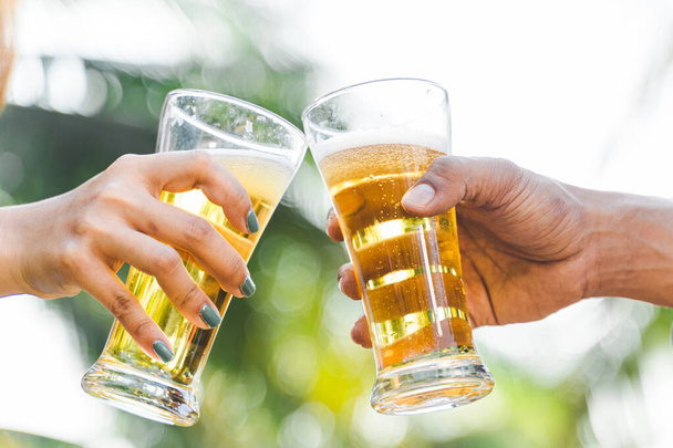 Καλλιεργημένη φωτογραφία ανθρώπων που κρατούν ποτήρια μπύρας και γιορτάζουν στην υπαίθρια καλοκαιρινή κατασκήνωση. Φίλοι clinking μπουκάλι μπύρα κατά τη διάρκεια κάμπινγκ εξωτερική - Φωτογραφία, εικόνα