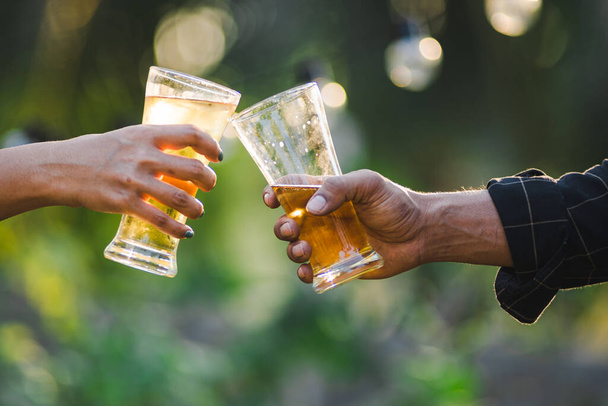 Cropped shot of people holding beer glasses celebrating in the summer camping party outdoor. Friends clinking bottle of beer during camping outdoor - Foto, Bild