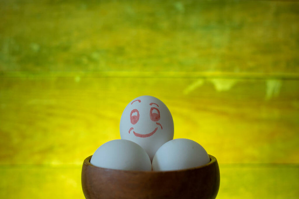 Tahta bir tabakta beyaz renkli yumurtalar. Gülen surat. renkli arkaplan - Fotoğraf, Görsel
