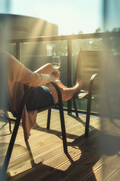 Kobieta siedzi i delektuje się białym winem na balkonie. - Zdjęcie, obraz