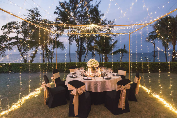 Ustawienie stołu do ceremonii ślubnej na świeżym powietrzu w nocy z widokiem na plażę, ozdobić kwiatami lotosu w stylu indyjskim - Zdjęcie, obraz