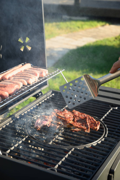 Beef steaks and sausages on grill. Barbecue backyard party. Outdoors. - 写真・画像