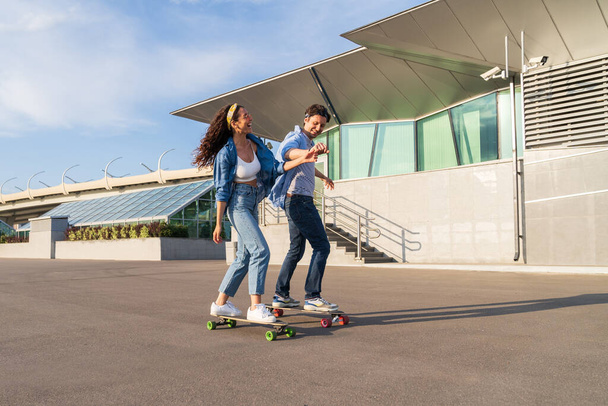 Joyful koppel op date longboarding samen: hipster guy skater leren lachende vrouw rijden skateboard - Foto, afbeelding