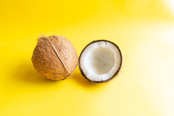Kokosový ořech, z něhož byla odstraněna slupka a půlka kokosového ořechu s krunýřem na žlutém pozadí a použitým selektivním ostřením. - Fotografie, Obrázek